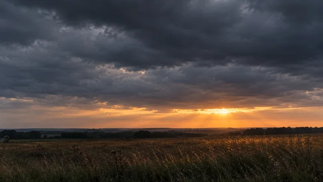 A heavy overcast sky above a flat empty field, one seam of light along the horizon