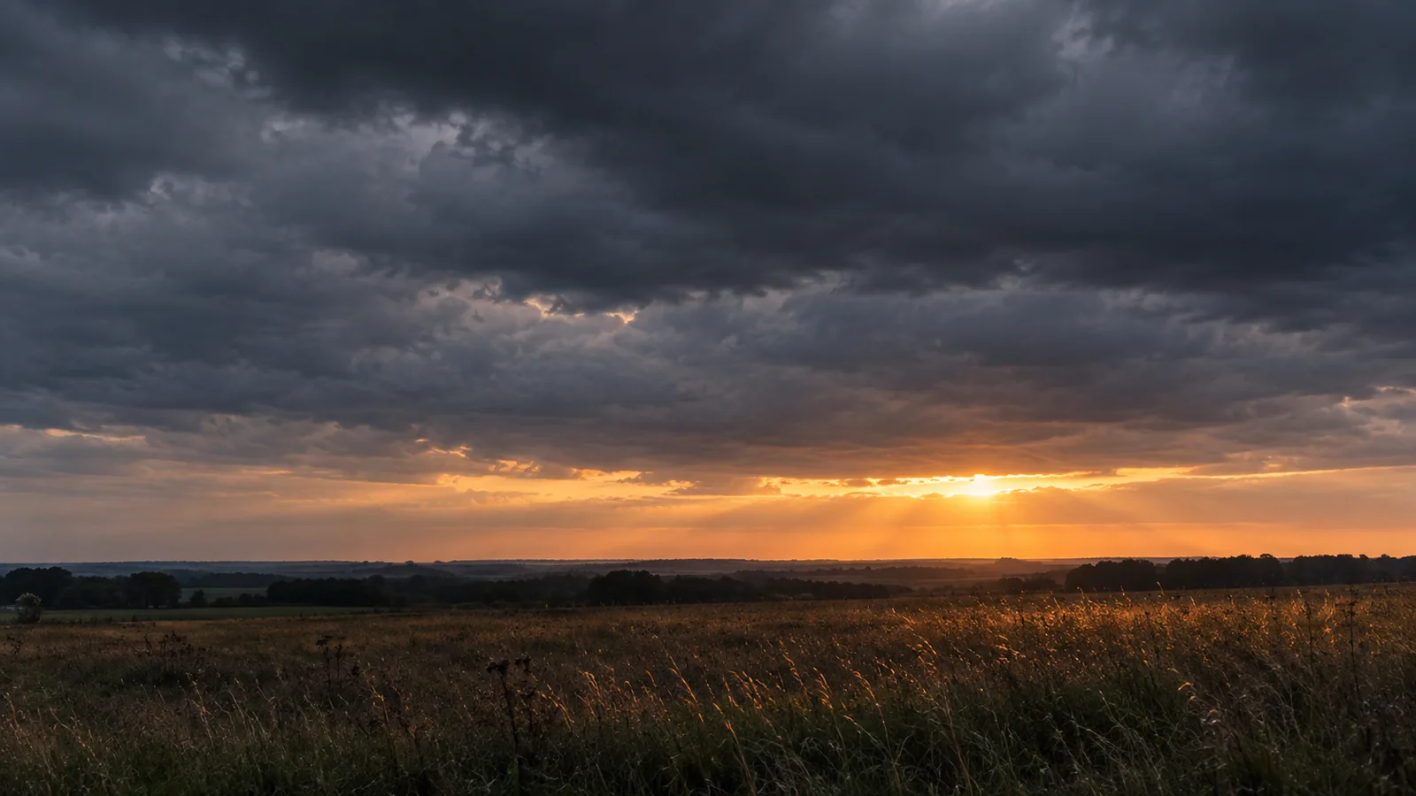 A heavy overcast sky above a flat empty field, one seam of light along the horizon