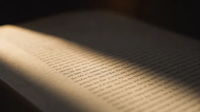 An open book on a table, one page lit by low raking sunlight