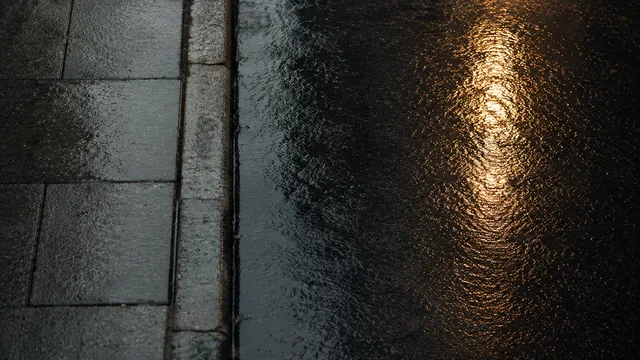 Wet paving stones at night holding the long reflection of a street lamp